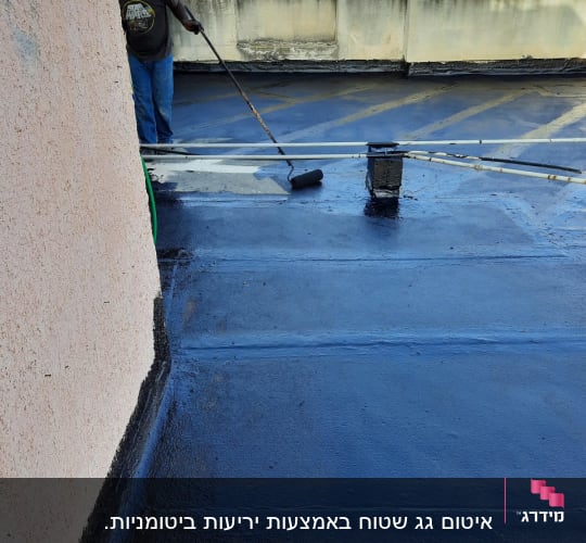 אדם מיישם חומר איטום על גג בעזרת רולר.